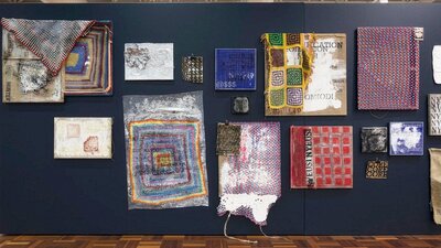 A series of mixed media artworks made from crochet, paint, hessian, hanging on a black wall