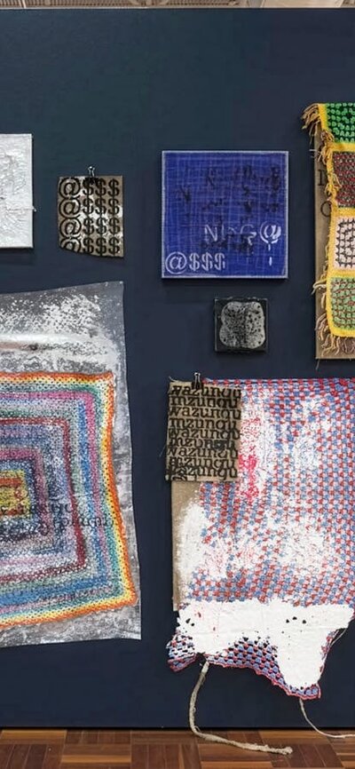 A series of mixed media artworks made from crochet, paint, hessian, hanging on a black wall