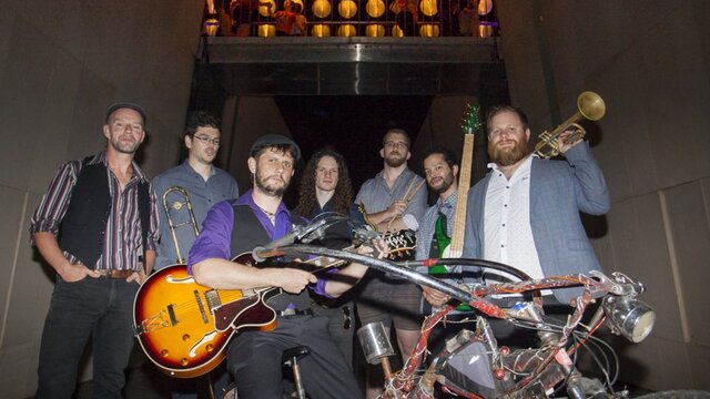 Photo of the artist, East Row Rabble 7 musicians in a laneway under lanterns holding their instruments. One is sitting on a bike.