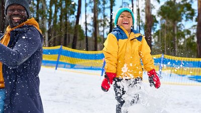 Father and son playing in the snow. Snow is sparaying around them as they laugh.
