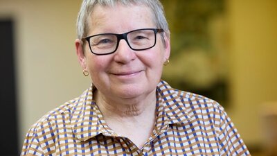 A short haired woman with glasses in a checkered shirt smiling at the camera