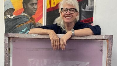 Person standing behind a large silkscreen with 2 posters on the wall behind themge silk