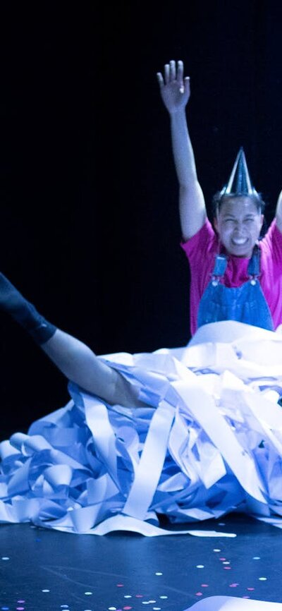 Woman wearing a bithday hat sitting in a pile of toilet paper