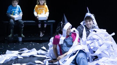 Man and woman on the floor covered in toilet paper with kids wearing birthday hats in the background
