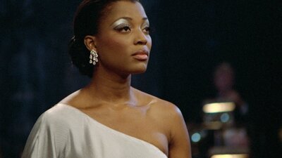 Woman stands with strong eye makeup looking to the right in an off the shoulder white top
