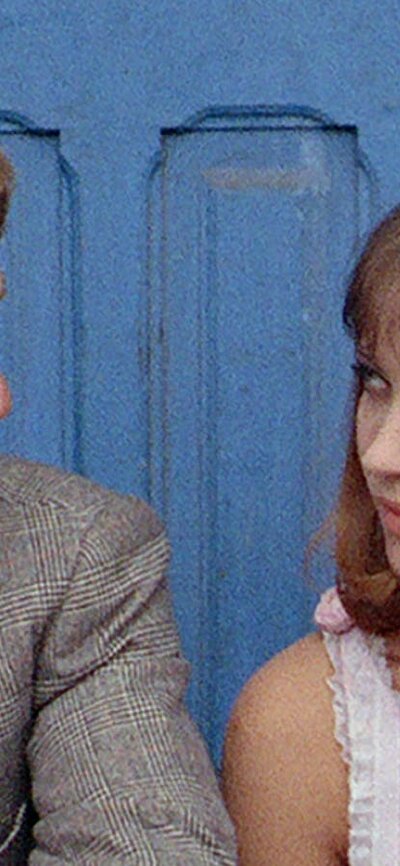 man in suit with red tie sitting on left and woman sitting on right looking at each other