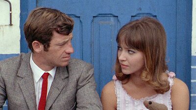 man in suit with red tie sitting on left and woman sitting on right looking at each other