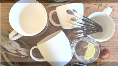 Art workshop samples. Ceramic mugs awaiting glazing with paint brushes and gin and tonic
