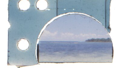 Skye Thompson, Sun Bake, 2024 A damaged and partially cropped 35mm film strip showing a serene ocean scene with a distant shorelin