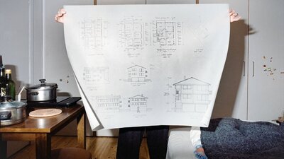 The Bees and the Ledger woman holding an architectural drawing in a bedroom