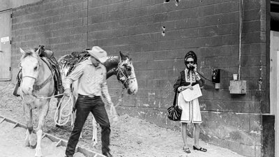 black and white photo of texas in the 170's. a woman is at an old phone booth and cowboys lead horse
