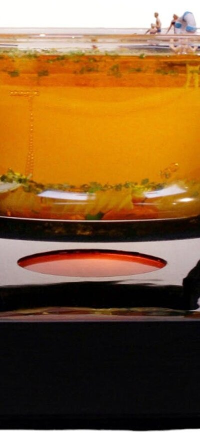 Glass bowl filled with amber coloured resin with miniature people inside