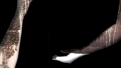 A darkroom print of two shadows of hands with multi coloured drips and chemical reactions