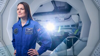 A woman at a space station wearing a blue astronaut uniform