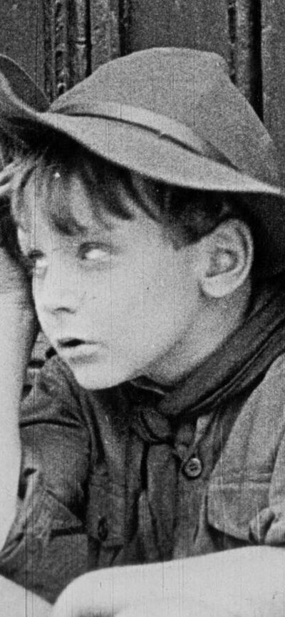 Black and white image of young boy sitting down with a hand on his face rolling his eyes