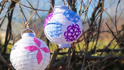 two white lanterns with colourful winter cutout patterns