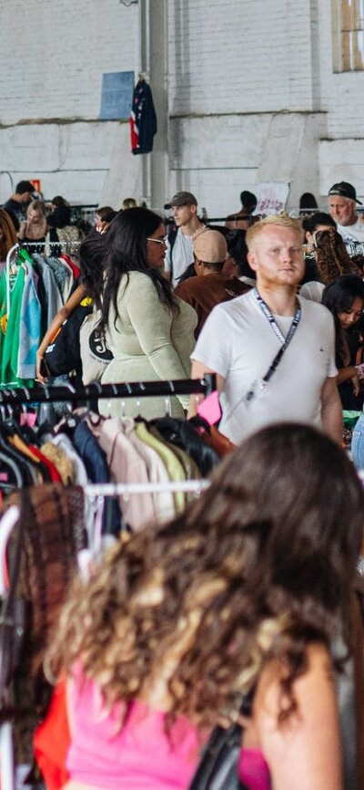 pictured is a view of the market with lots of racks of clothes and people