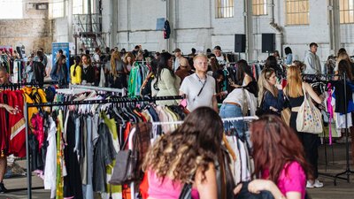 pictured is a view of the market with lots of racks of clothes and people