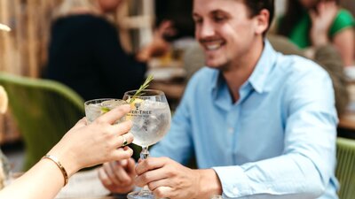 Two people clinking gin and tonic glasses across a restaurant table