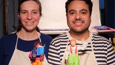 A woman and a man posing while holding painted figurines with craft supplies