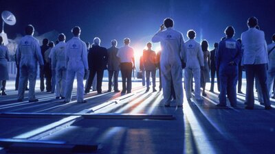 Blue glowy image with the backs of people standing in white lab coats