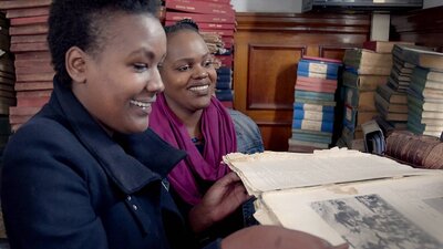 Two women reading books in a room full of books and manuscripts