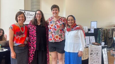 Four women stand before market stalls at the For Purpose Markets