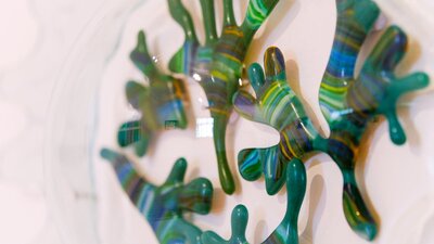 Close up of a glass sculpture of seaweed made from greens inside a transparent glass bubble