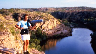 A film crew member recording sound with a gorge and rocky landscape in the background.