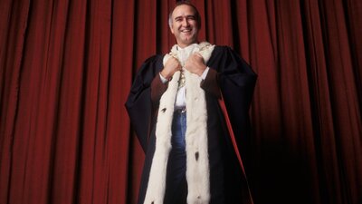 Man stands wearing a royal cape smiling at camera