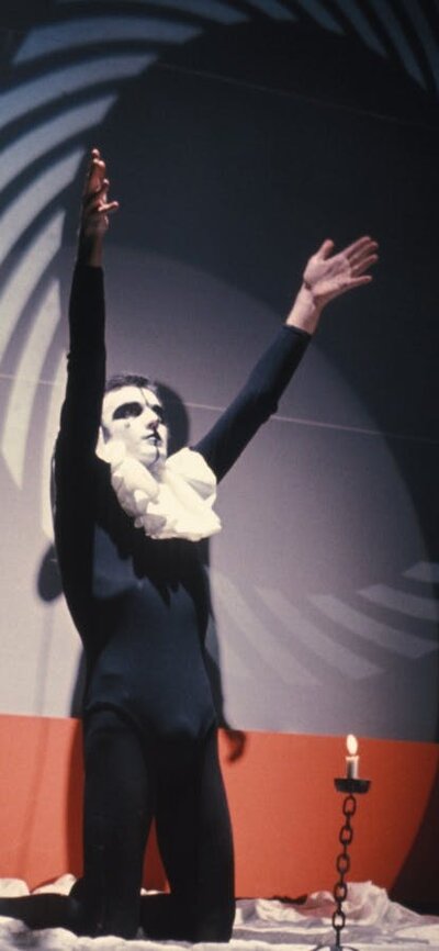 Band on stage wearing black and white costumes with main singer on his knees