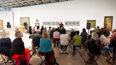 Photo of a group of people sitting in a gallery listening to someone talk