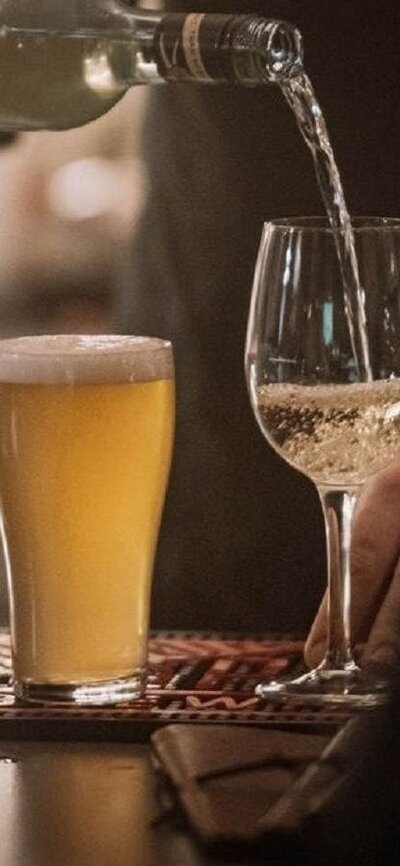 Wine being poured into glass, next to full schooner of beer