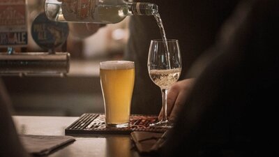 Wine being poured into glass, next to full schooner of beer