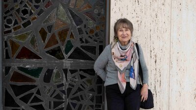 An woman with short gray hair stands smiling beside a decorative mosaic wall.