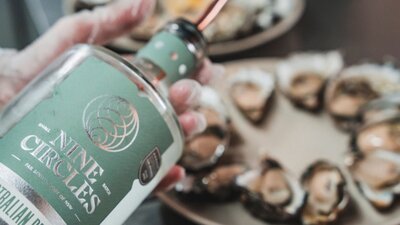 Someone holding a bottle of gin in front of a plate of oysters