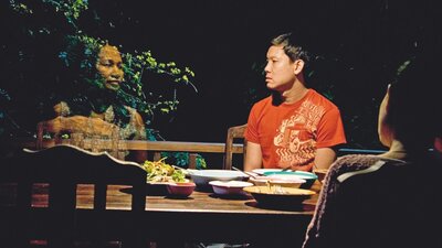 Man sitting around table at night with a ghost figure of a woman next to him