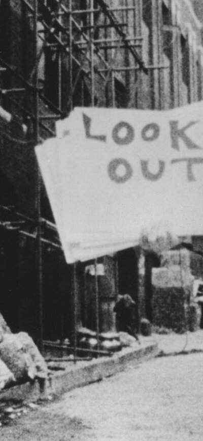 Black and white photo of Bob Dylan holding a poster that says look out!