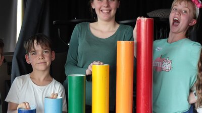 Three kids playing with rainbow percussion tubes