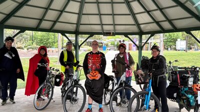 People in Halloween costumes stand beside their bikes.