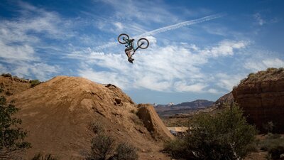 Woman on motorcycle doing a jump and upside down, set in mountains