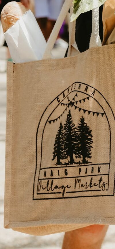 A peson holding a hessian Haig Park Village Market bag filled with bread and produce