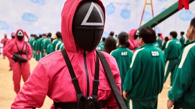 A Netflix Original Series. Squid Game © 2021 Netflix. All Rights Reserved A still shot from movie Squid Game. Men in pink and green suits.