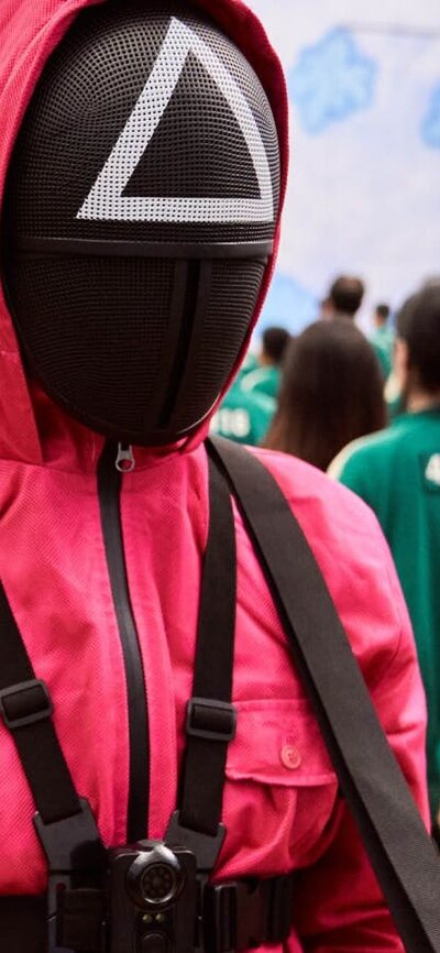 A still shot from movie Squid Game. Men in pink and green suits.