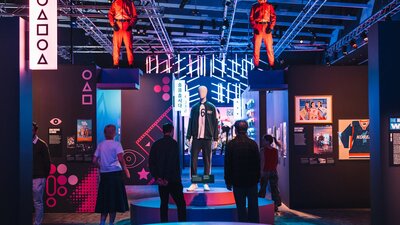 Exhibit with mannequins in red jumpsuits, surrounded by neon lights and displays.