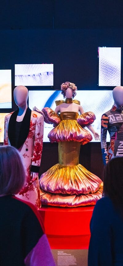 A dimly lit exhibit showcases mannequins dressed in Korean fashion on a red circular platform.