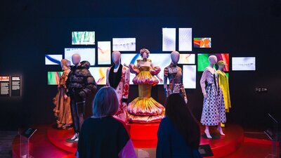 A dimly lit exhibit showcases mannequins dressed in Korean fashion on a red circular platform.