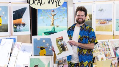 Beau Wylie standing in front of his stall at the Handmade Market Canberra holding his art