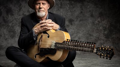 Harry Manx sitting down, holding stringed instrument