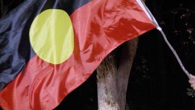 First Nations Flag on a stick, being waved in the darkness